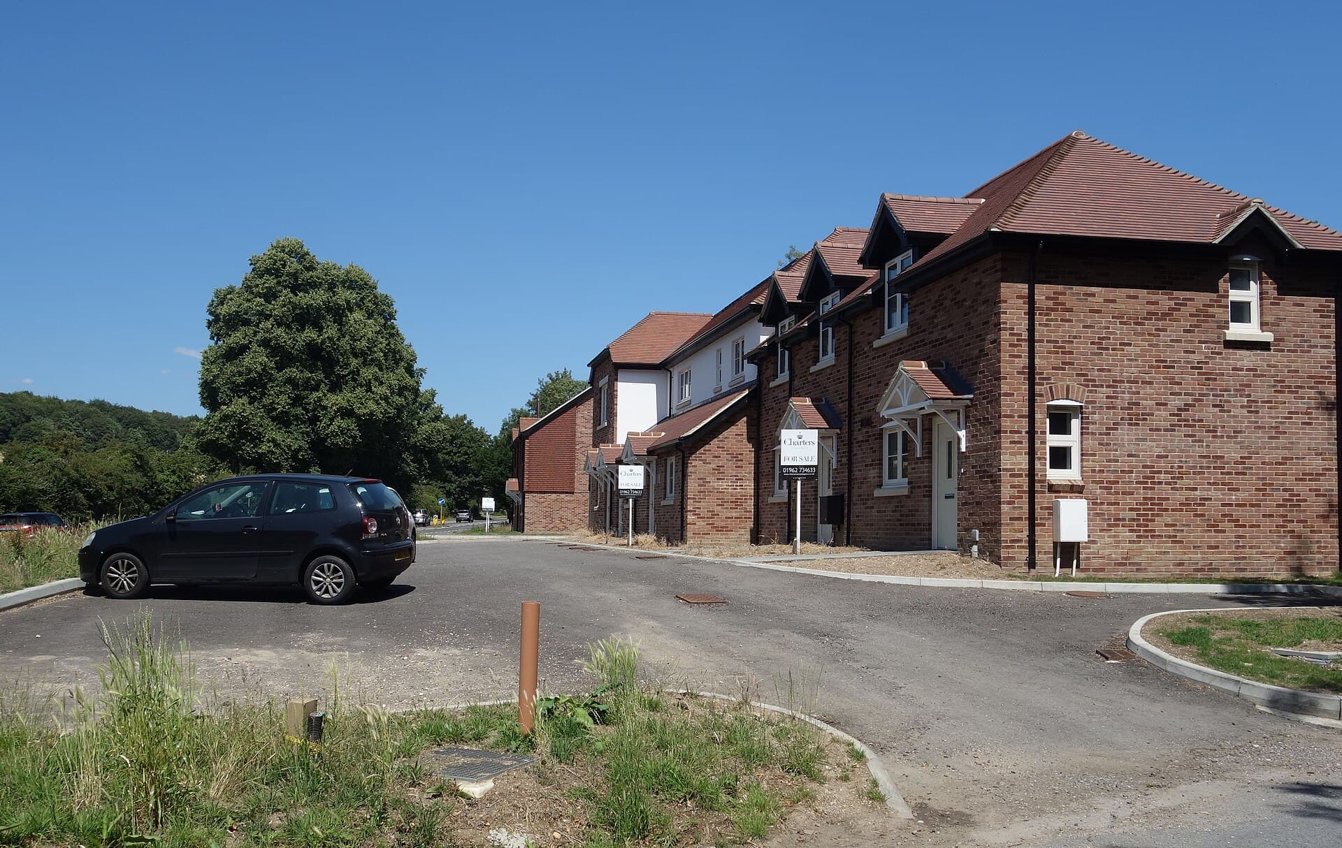 A row of newly built brick houses on a quiet estate road, each with an estate agent's For Sale board outside, under a clear blue sky
